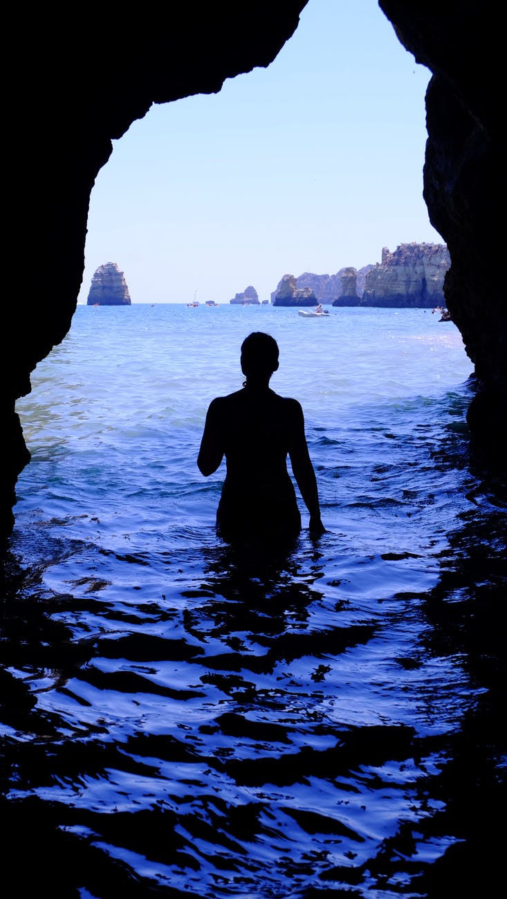 silhouette of woman at blue sea inside black cave during daytime